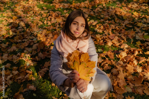 cute brunette in a beige coat with leaves in her hands on a background of autumn leaves