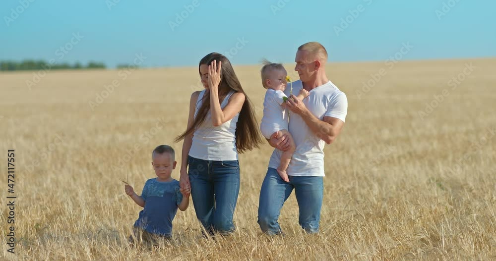 Young parents on a walk with young children in a wheat field. Dad plays with the baby, happy fatherhood. Mom and dad are walking with their son and daughter on the golden field, blue sky. 4k, ProRes Young parents on a walk with young children in a wheat field. Dad plays with the baby, happy fatherhood. Mom and dad are walking with their son and daughter on the golden field, blue sky. 4k, ProRes