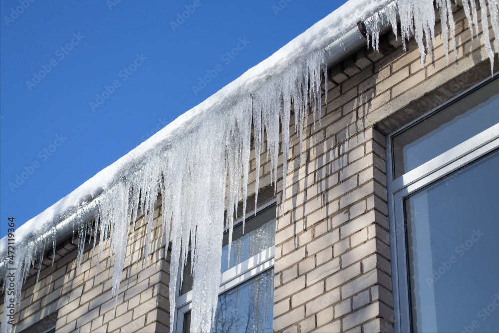 Bright sunny day. Long, shiny icicles on the roof of the house. Frosty morning. Dangerous place of falling icicles.