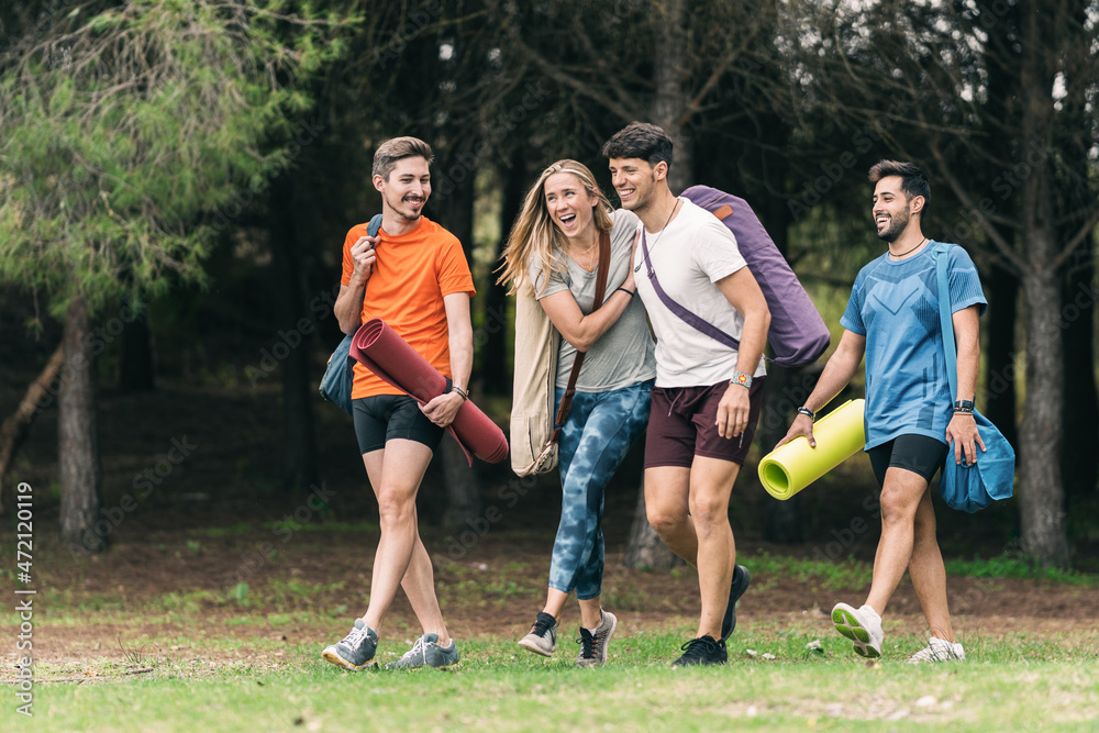 Smiling friends joking on their way to do yoga in a forest Smiling friends joking on their way to do yoga in a forest