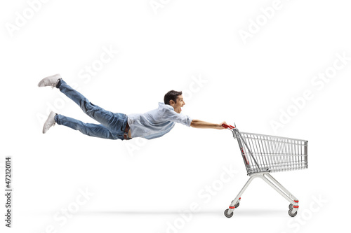 Slika na platnu Full length shot of a casual young man flying and holding an empty shopping cart