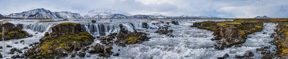 Season changing in southern Highlands of Iceland. Picturesque waterfal Tungnaarfellsfoss panoramic autumn view.  Landmannalaugar mountains under snow cover in far.