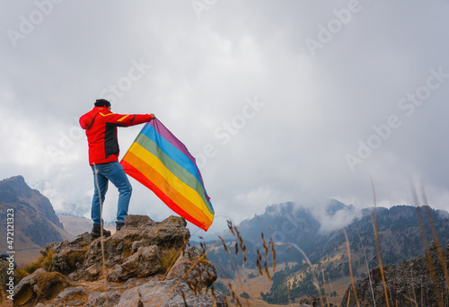 Man standing on top of the hill and holding the LGBT pride flag