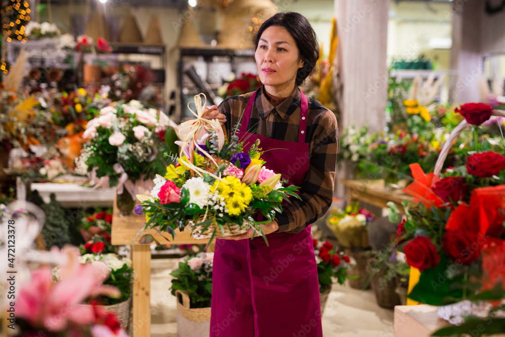 Positive female florist in apron holding bouquet at flower shop