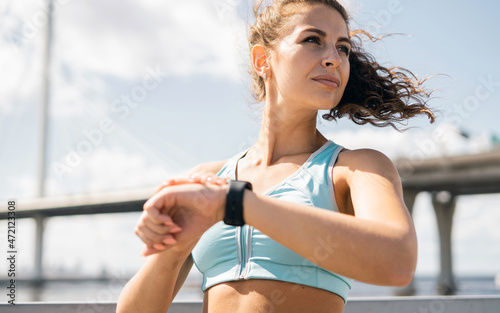Confident woman running city embankment, athletic figure, comfortable fitness clothes. A smart watch for heart rate counting. A sporty lifestyle, the coach takes a break.
