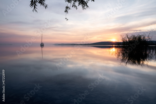 a sailing boat at sunset on a calm lake