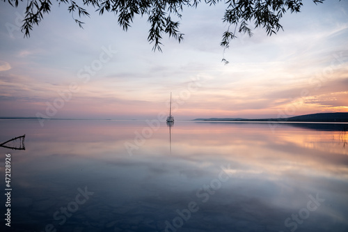 a sailing boat at sunset on a calm lake