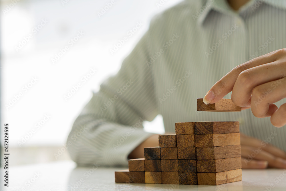 Young woman's hand placing wooden blocks on stairs and journey to successful business growth idea Young woman's hand placing wooden blocks on stairs and journey to successful business growth idea