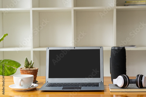 Laptop computer and coffee mug with headphones, books, speakers on a businessman's desk.