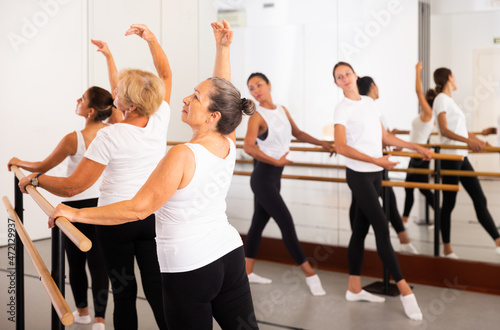 Group of people doing exercises using barre in gym with focus to fit athletic toned woman in foreground in health and fitness concept