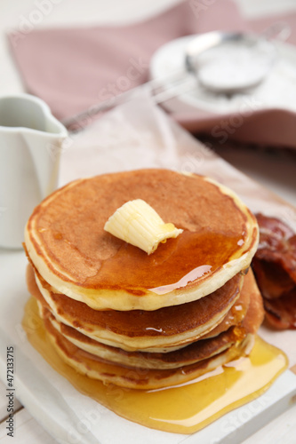 Delicious pancakes with maple syrup, butter and fried bacon on white table, closeup