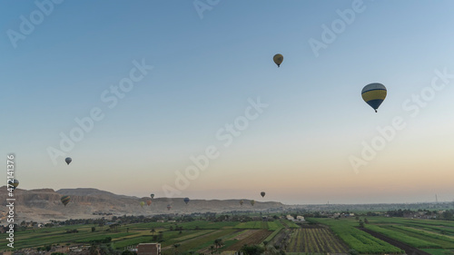 Lots of colorful balloons are flying in the morning sky. Below is the Nile Valley with cultivated fields. A picturesque mountain range in the distance. Egypt. Luxor