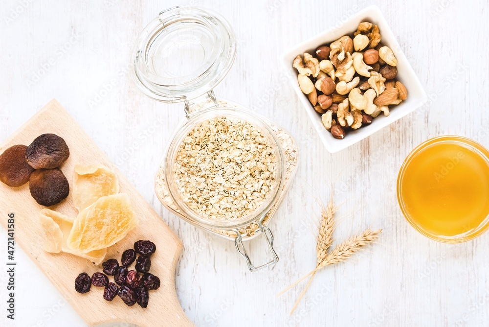Top view of raw ingredients for homemade granola preparation - oats, nuts, honey and dried fruits. Healthy eating.