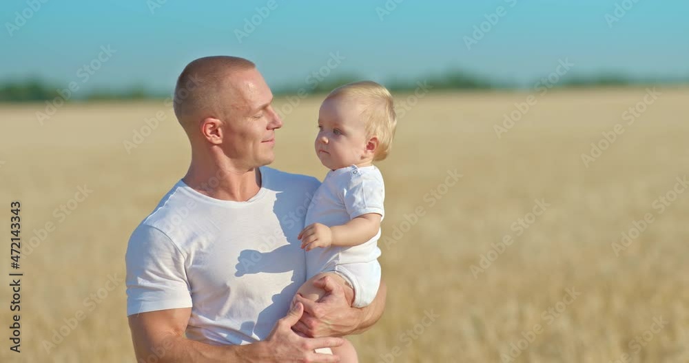 Young father carries a baby daughter in his arms, a walk in a wheat field. Father kisses the baby, happy fatherhood and childhood. Family values. 4k, ProRes Young father carries a baby daughter in his arms, a walk in a wheat field. Father kisses the baby, happy fatherhood and childhood. Family values. 4k, ProRes