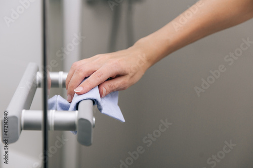 Cleaning glass door handles with an antiseptic wet wipe. Woman hand using towel for cleaning home room door link. Sanitize surfaces prevention in hospital and public spaces against corona virus