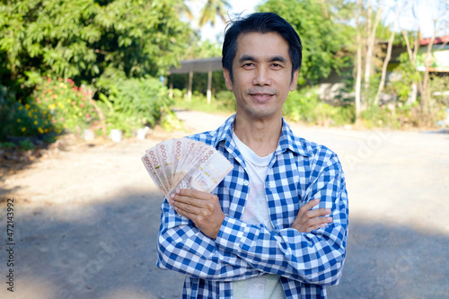 Fototapeta Asian farmer wear blue shirt holding Thai baht banknote money and cross arm smil