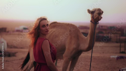 Blonde girl walking towards a camel while a trip at the desert of UAE Dubai photo
