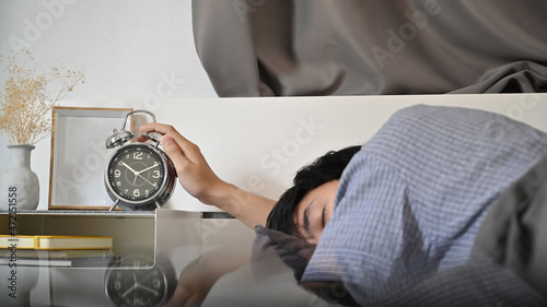 Canvas Print Sleepy man young man lying on the bed and stopping alarm clock.