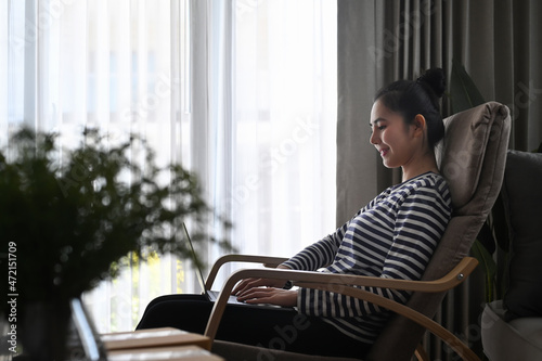 Beautiful young woman sitting in living room and surfing internet with laptop computer.