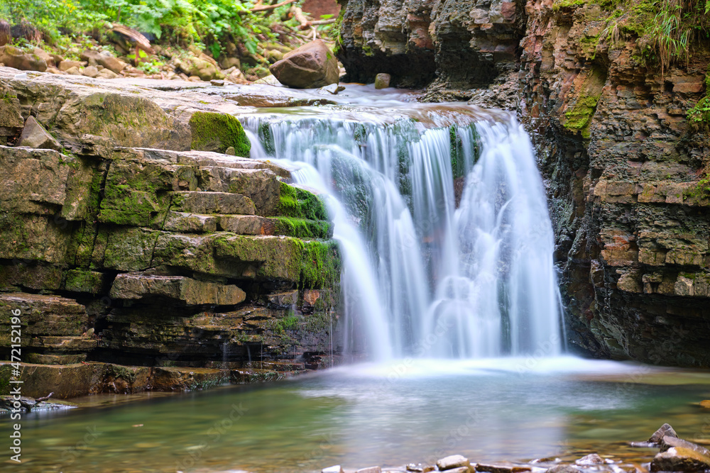 Fototapeta premium Amazing landscape of beautiful waterfall on mountain river with white foamy water falling down from rocky cliff in summer rainforest