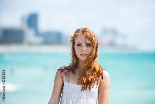 Sunner portrait of redhead beautiful girl at beach. Young tanned woman enjoying breeze at seaside. Carefree woman smiling with sea ocean in background.