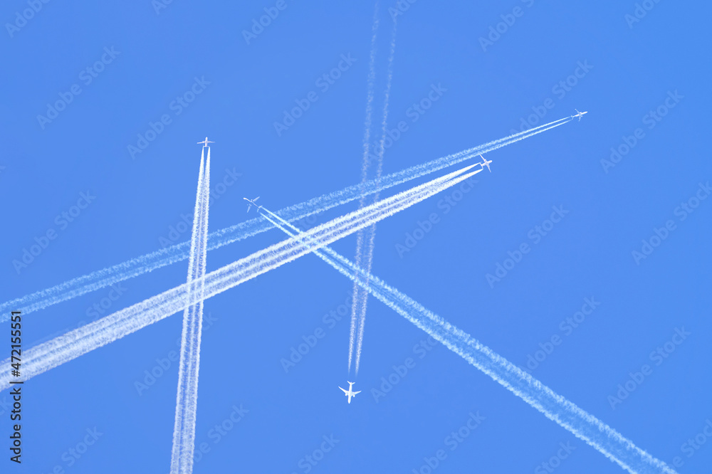 Many distant passenger jet planes flying on high altitude on clear blue sky leaving white smoke trace of contrail behind. Busy air transportation concept