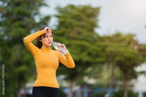 tired woman drinking water after running in park