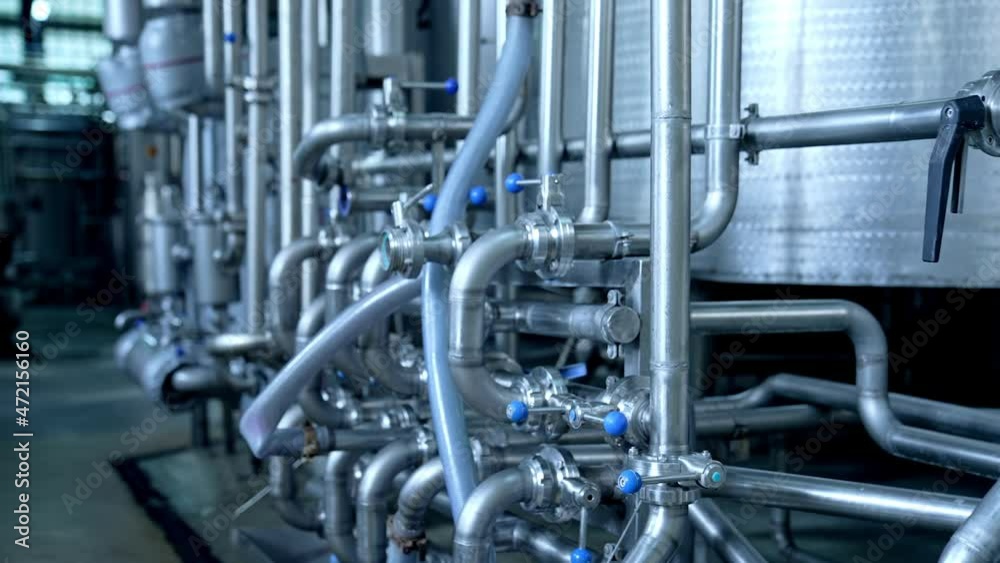 Numerous pipes crossing with each other at modern milk factory enterprise. Pipelines with valves and faucets. Close up with gradual distancing.