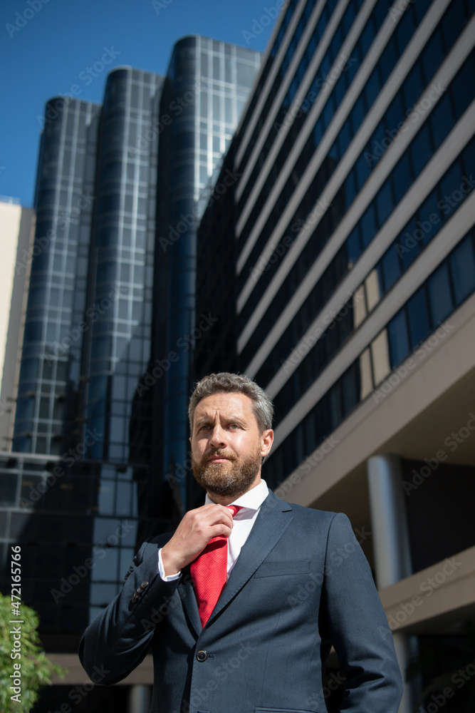 Business man in blue suit tying the necktie outdoor. Well dressed businessman on city office building. Business man in blue suit tying the necktie outdoor. Well dressed businessman on city office building.