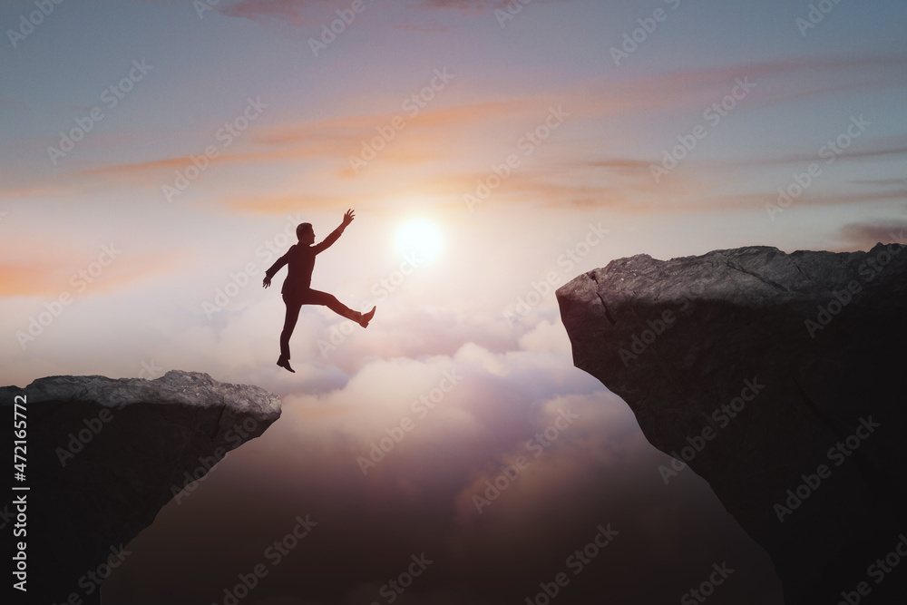 Man jumping from cliff on beautiful sky background. Gap, leap, risk, challenge and success concept.