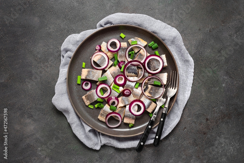 Salted herring with onions in a plate on a dark grunge background. Top view, flat lay. photo