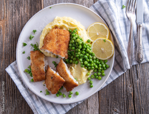 Traditional breaded fish with mashed potatoes and green peas on a plate