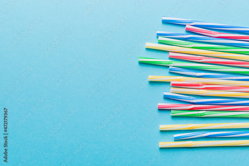 Fototapeta premium Heap of colorful plastic drinking straws on Colored background, flat lay. Copy Space for text