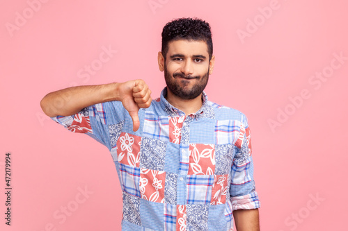 Fotografi Portrait of young adult man in blue shirt criticizing bad quality with thumbs down displeased grimace, showing dislike gesture, expressing disapproval