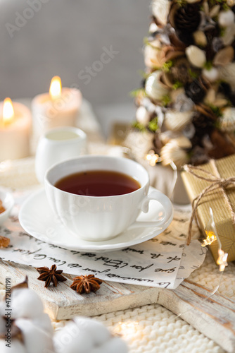 Cozy winter morning at home. Hot tea in a cup, knitted plaid, gifts, candles, christmas tree and modern interior details. Winter Flat lay, cozy still life composition, hygge, menu