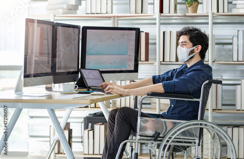 A bearded trader investor wear face mask who uses a wheelchair typing information on computer study market working at home office buy sell stock trading for customer
