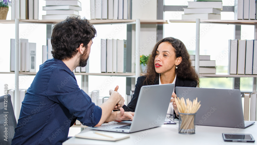Caucasian bearded businessman trainee working with African American businesswoman manager trainer in formal suit sitting teaching coaching at working desk Caucasian bearded businessman trainee working with African American businesswoman manager trainer in formal suit sitting teaching coaching at working desk