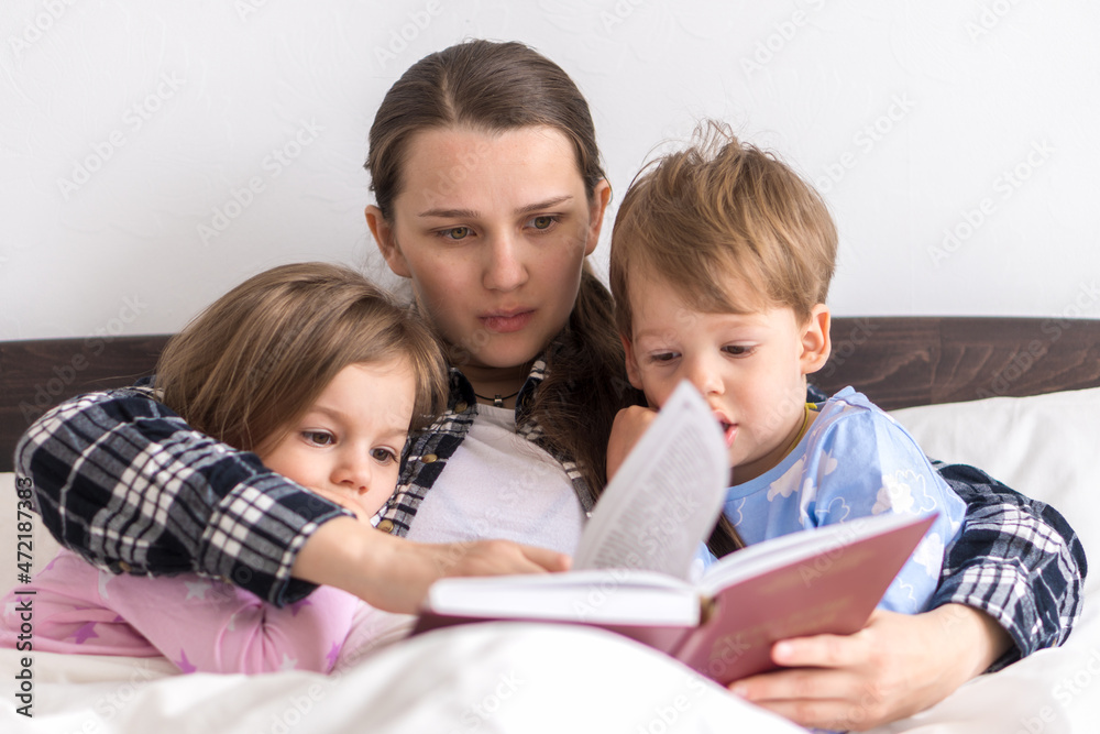 happy family. Close up loving mother lying with daughter son two kids pajamas in bed children reading interesting storybook, preschool smiling kid girl enjoy fairytale before go to sleep good pastime happy family. Close up loving mother lying with daughter son two kids pajamas in bed children reading interesting storybook, preschool smiling kid girl enjoy fairytale before go to sleep good pastime