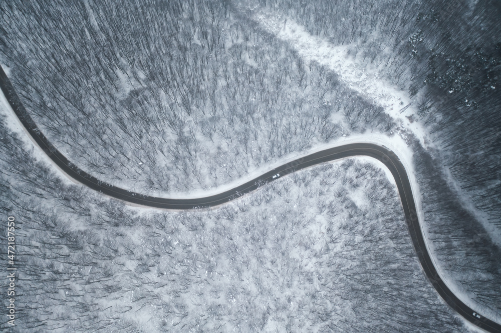 Top view with curvy mountain road in snow covered forest.