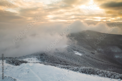 Beautiful winter landscape with snow-capped mountain peaks and frozen bushes on the ridge at sunrise.