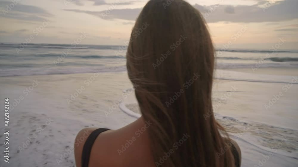 Arc shot of young beautiful woman recording video on smartphone of her little son walking along sea coast at sunset