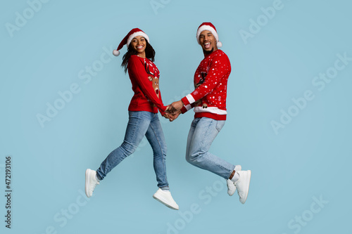 Loving black couple in Santa hats jumping up together
