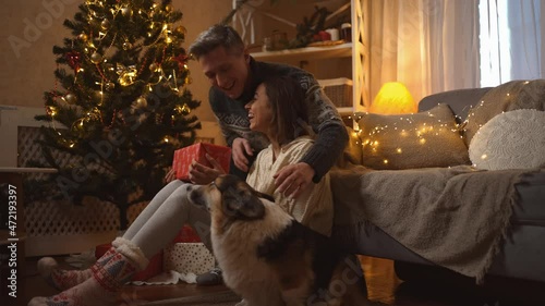family celebrating Christmas with their cute Corgi dog at festive decorated cozy house. happy smiling woman getting red gift box from loving man on New Year celebration at home photo