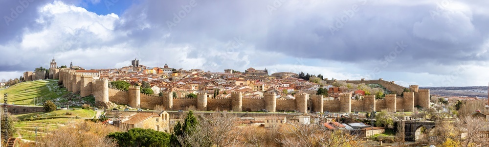 Panoramic view of the Spanish city Avila surrounded by its medieval walls with a dark and cloudy sky on a bad weather day