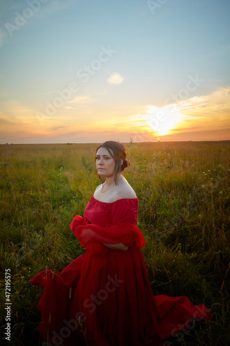 Fat plump chubby pleasant woman or girl in elegant red dres in green grass field. model posing outdoors on nature in a day or a evening