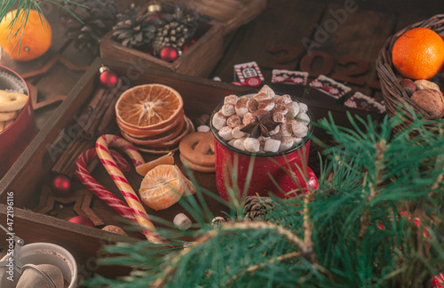 In a wooden tray there is a mug with marshmallows and New Year s attributes