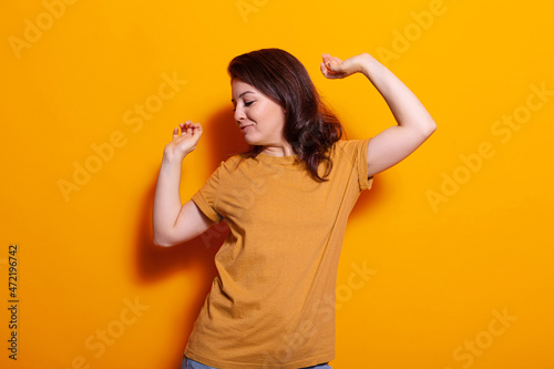 Young woman feeling joyful while moving in studio over orange background. Cheerful person smiling and doing dance moves, to have fun at casual photoshoot. Adult with energy dancing
