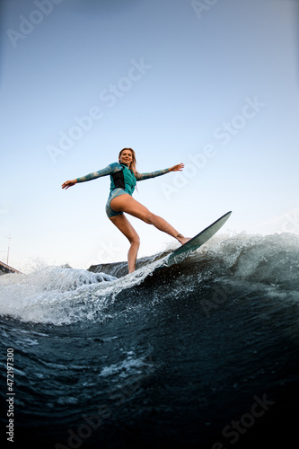 attractive smiling woman balancing on splashing wave on wakesurf.