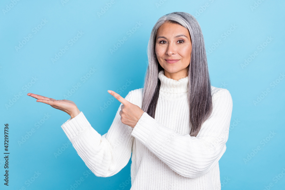 Photo of pretty mature woman indicate finger promotion offer advertise isolated over blue color background Photo of pretty mature woman indicate finger promotion offer advertise isolated over blue color background