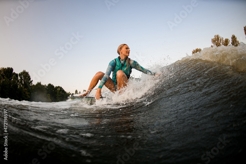 Fototapeta Naklejka Na Ścianę i Meble -  attractive woman sits on surf and rides the wave and touches the wave with one hand